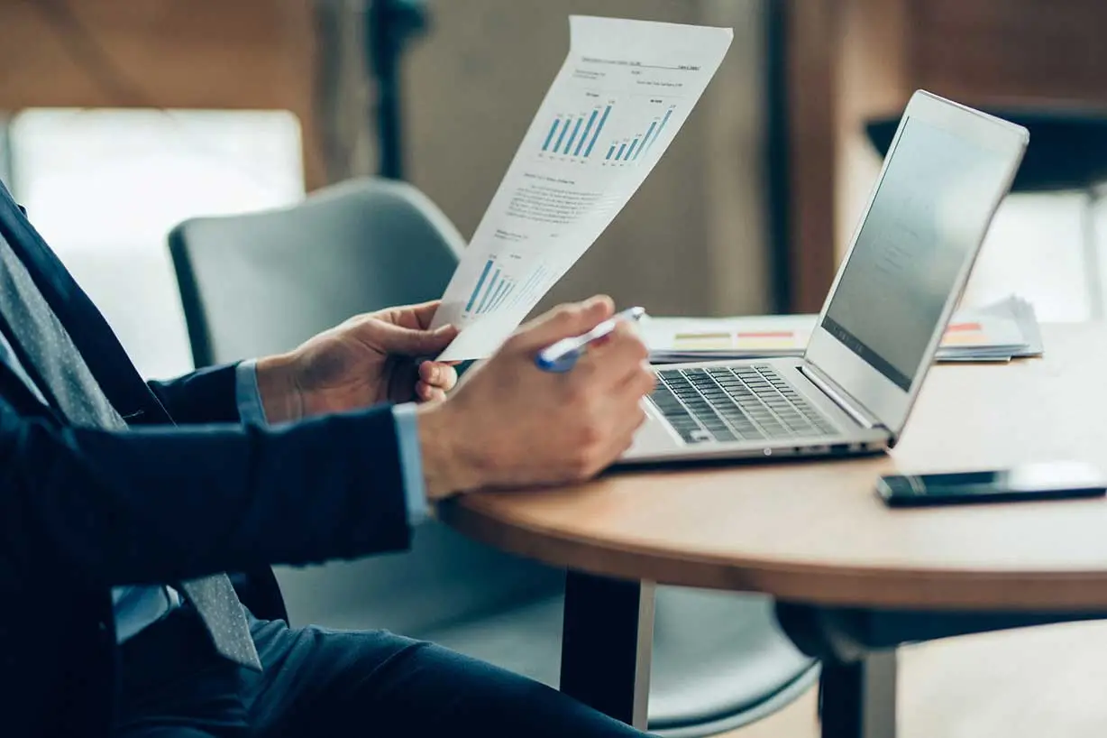 A smartly dressed man in an office comparing a two transport data sets using his laptop